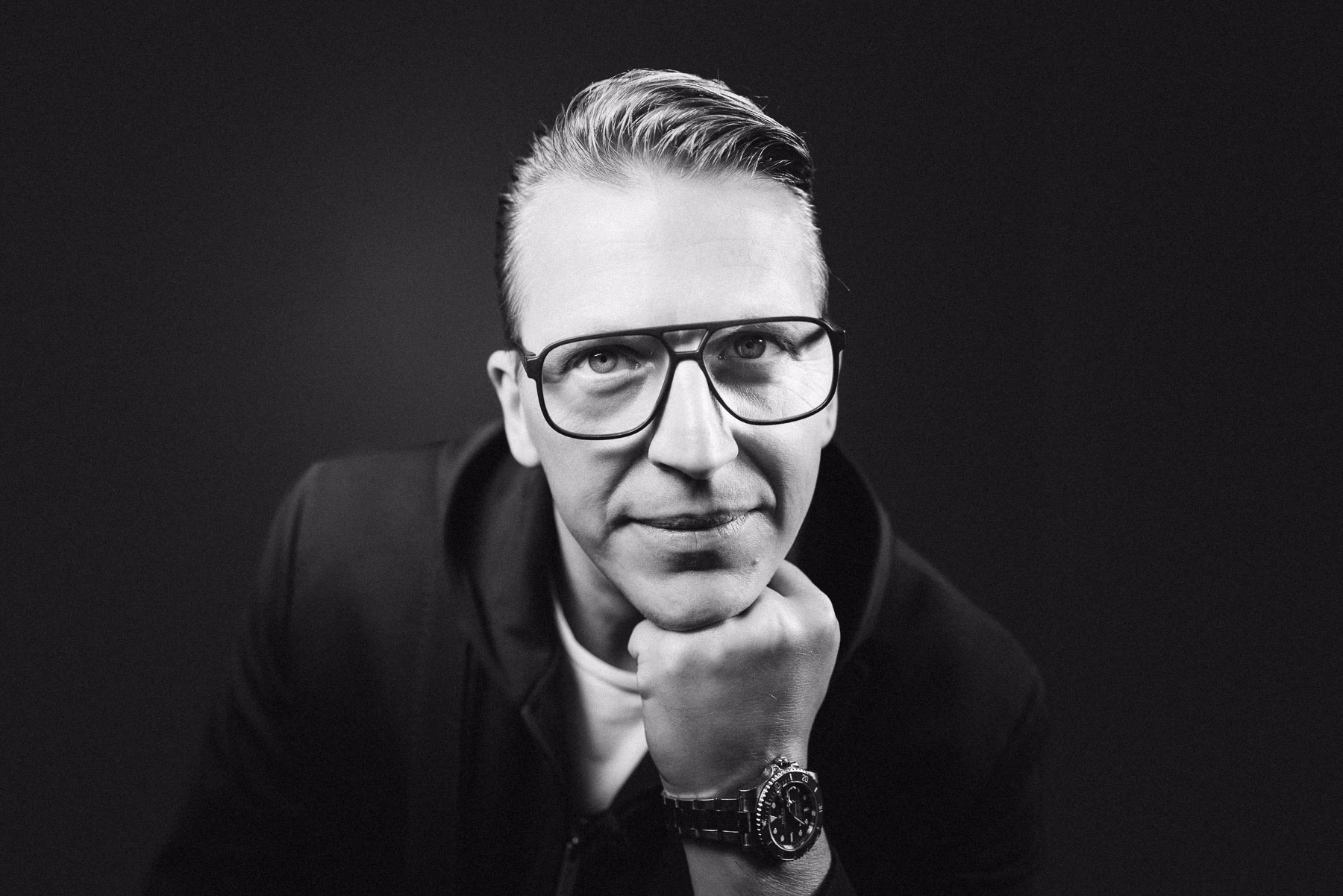 Mann mit Brille stützt Kinn auf die Faust, dunkler Studiohintergrund