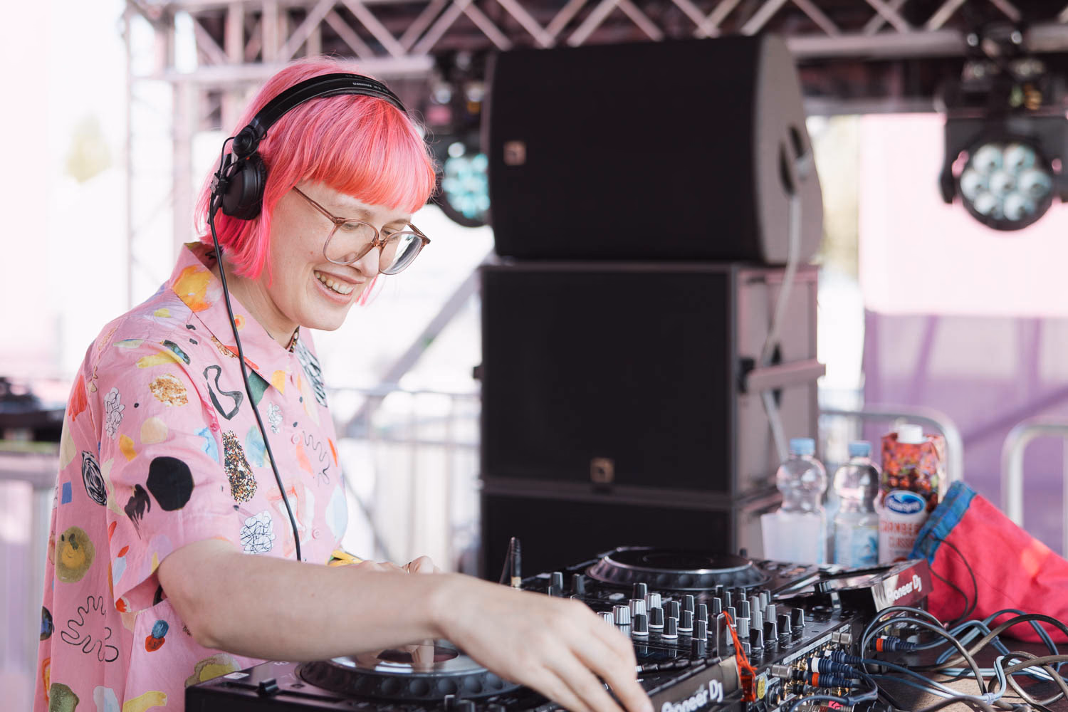 DJ mit rosa Haaren und Brille am Pult