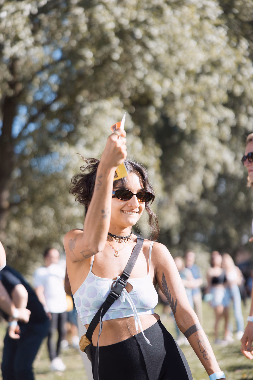 Festivalbesucherin mit Sonnenbrille hebt ihr Getränk